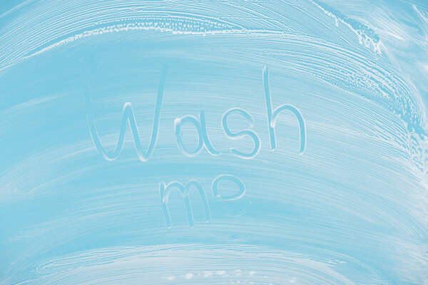 wash me handwritten lettering written on glass with white foam on blue background