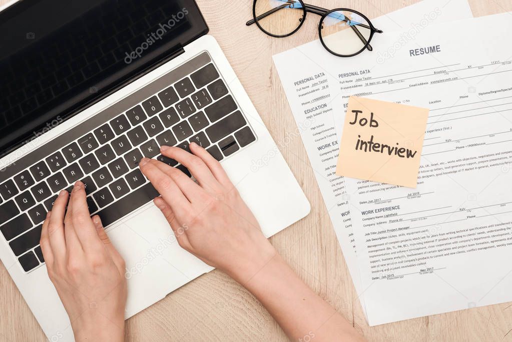 cropped view of recruiter typing on laptop keyboard near glasses, resume templates and sticky note with job interview lettering 