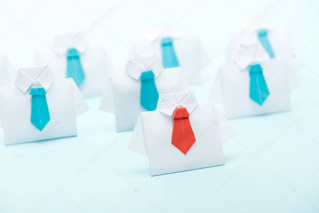 selective focus of origami white shirts with blue ties with one red on blue background, leadership concept