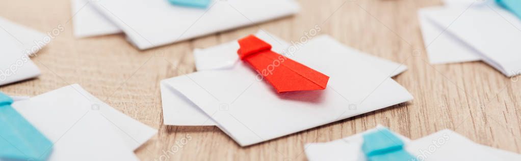 panoramic shot of origami white shirts with blue ties with one red on wooden surface