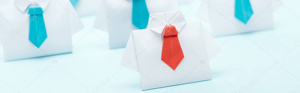 panoramic shot of origami white shirts with blue ties with one red, leadership concept