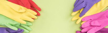 panoramic shot of colorful rubber gloves on green background with copy space clipart