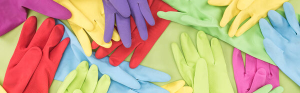panoramic shot of scattered multicolored rubber gloves on green background