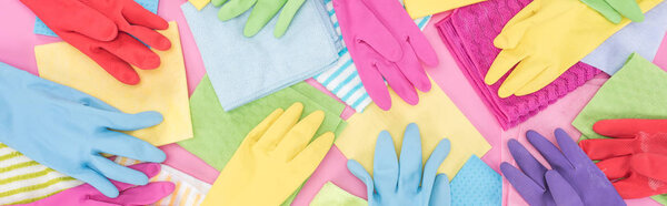 panoramic shot of scattered multicolored rags and rubber gloves on pink background