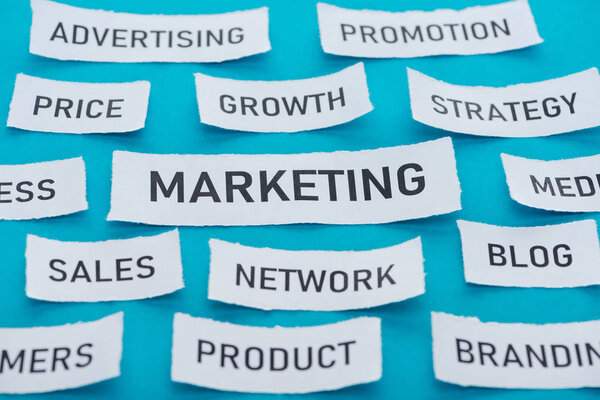 word marketing with components of marketing on pieces of paper on blue 