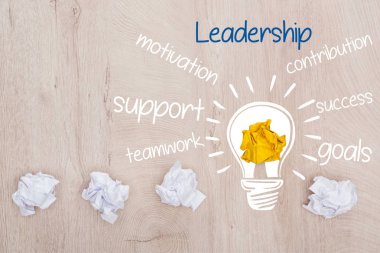 Buruşmuş kağıt toplarının üst görünümü, ampul ve liderlik, motivasyon, katkı, destek, başarı, takım çalışması, hedefler sözcüğü ahşap yüzey, iş kavramı