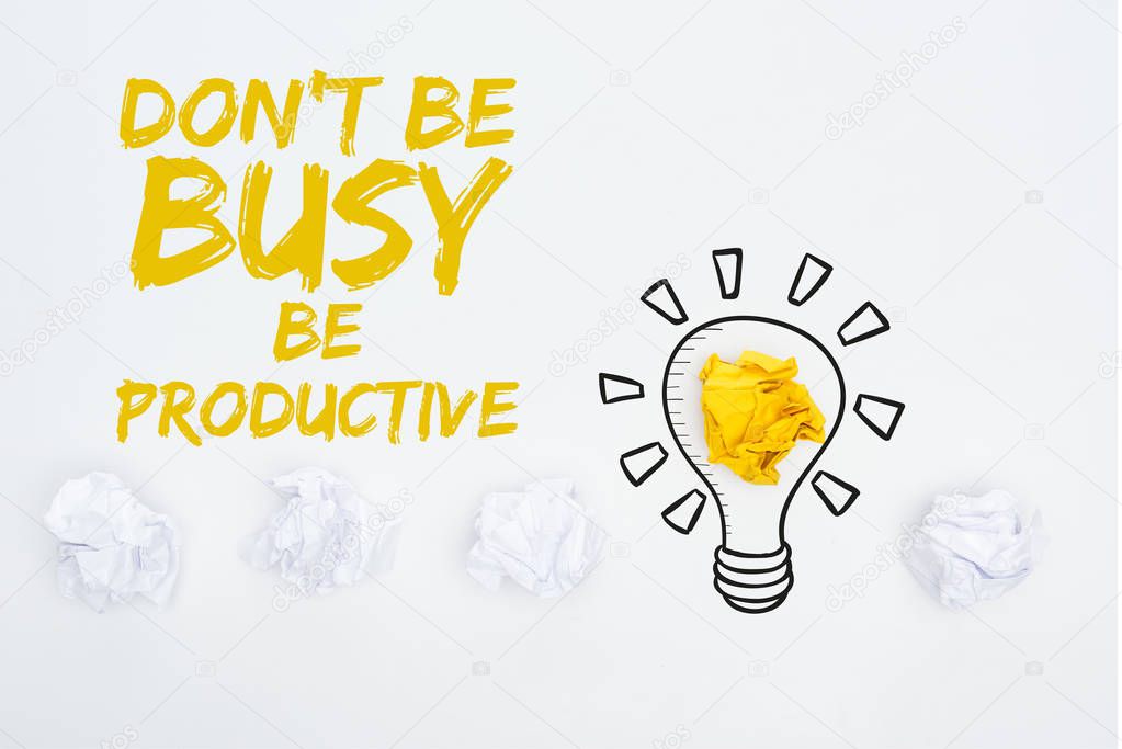 top view of crumpled paper balls, don't be busy be productive inscription and illustration of light bubble on white background, business concept