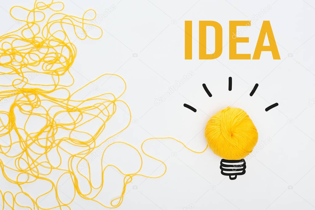 top view of yellow knitting ball near light bulb and idea inscription on white background, business concept