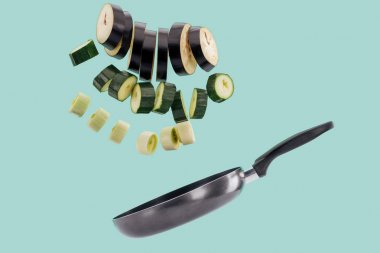 Sliced green organic tasty vegetables above frying pan isolated on turquoise  clipart