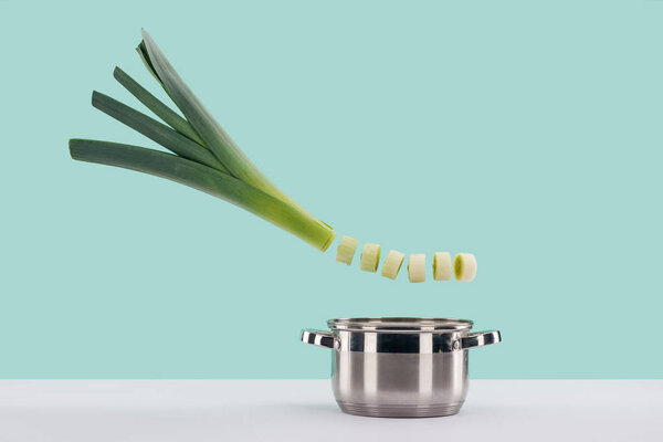 Green fresh sliced leek above saucepan on white surface isolated on turquoise 