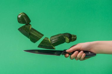 Partial view of woman holding knife with chopped organic zucchini isolated on green clipart
