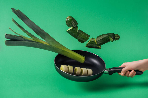 Cropped view of woman holding frying pan with delicious sliced organic vegetables on green background