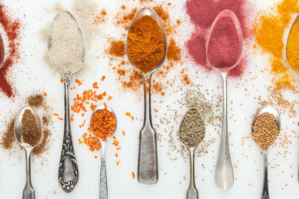верхний вид различных красочных специй в серебряных старых ложках на белом фоне
