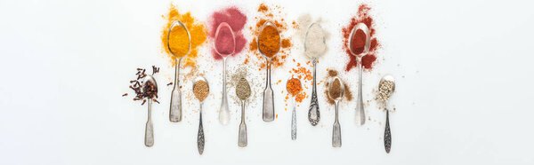panoramic shot of various colorful spices in silver spoons on white background 