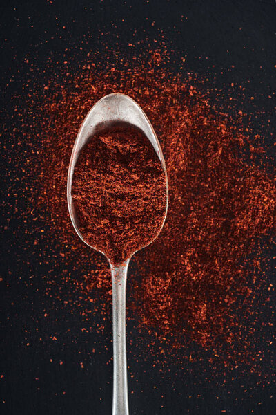 top view of paprika spice in silver spoon on black background