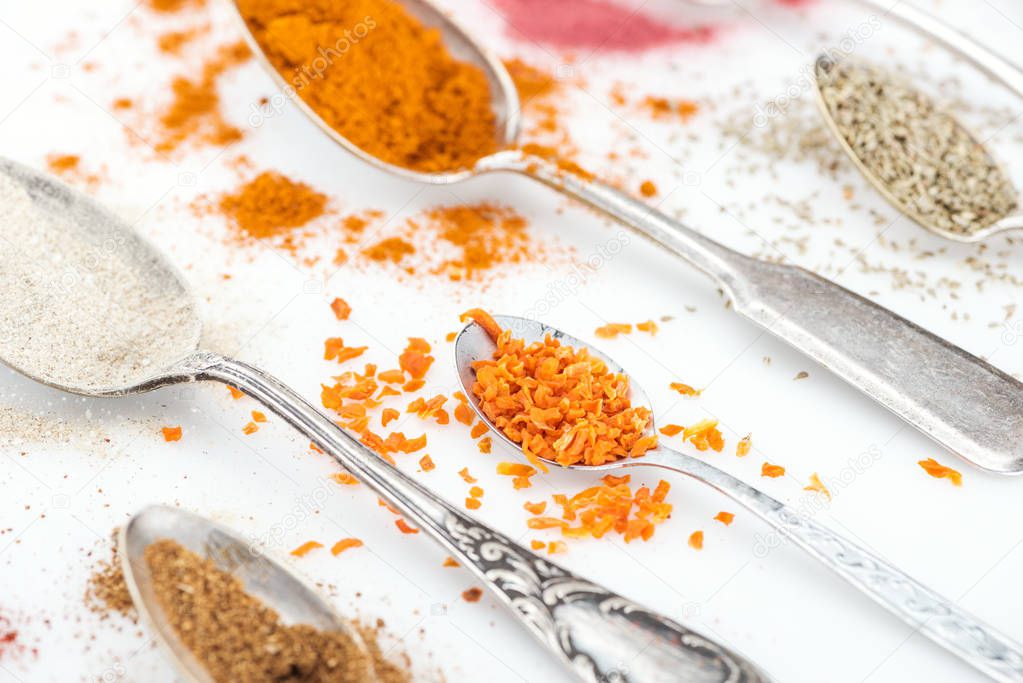 close up view of various bright spices in silver vintage spoons on white background