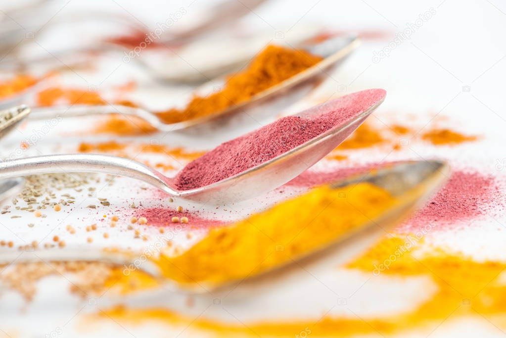 selective focus of colorful spices in silver spoons on white background