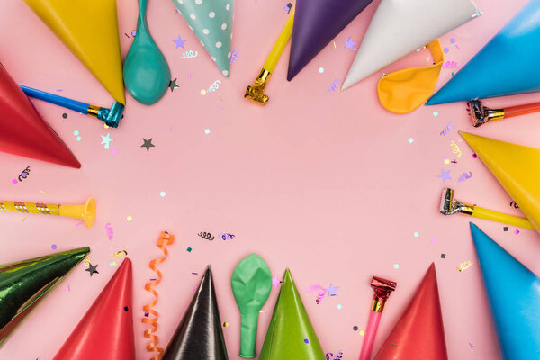 Top view of party horns, caps and confetti on pink background