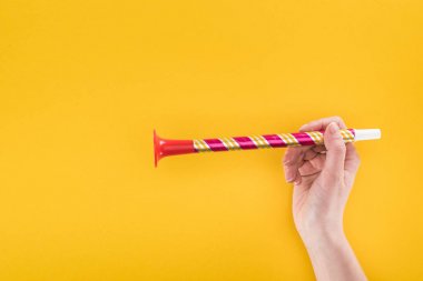 partial view of woman holding red party horn on yellow background clipart