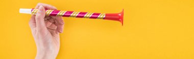 Panoramic shot of woman holding red party horn on yellow background clipart