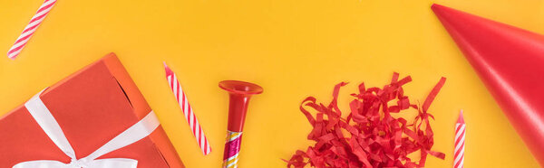 Панорамный снимок красной подарочной коробки, свечей и праздничного рога на желтом фоне
