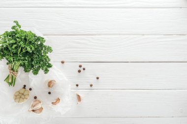 top view of garlic cloves, black pepper and parsley on white wooden table clipart