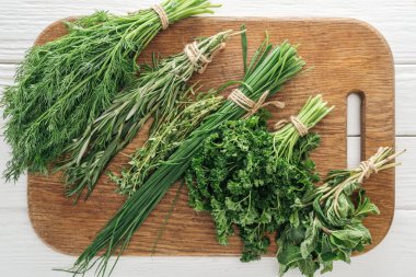 top view of parsley, rosemary, dill, green onion, basil and thyme on wooden chopping board clipart