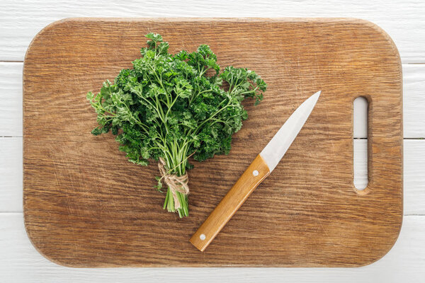 top view of green parsley and knife on wooden chopping board