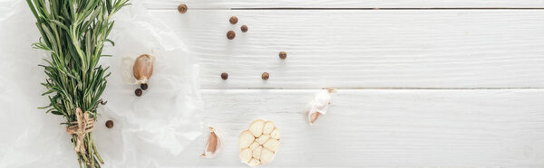 panoramic shot of garlic cloves, black pepper and rosemary on white wooden table