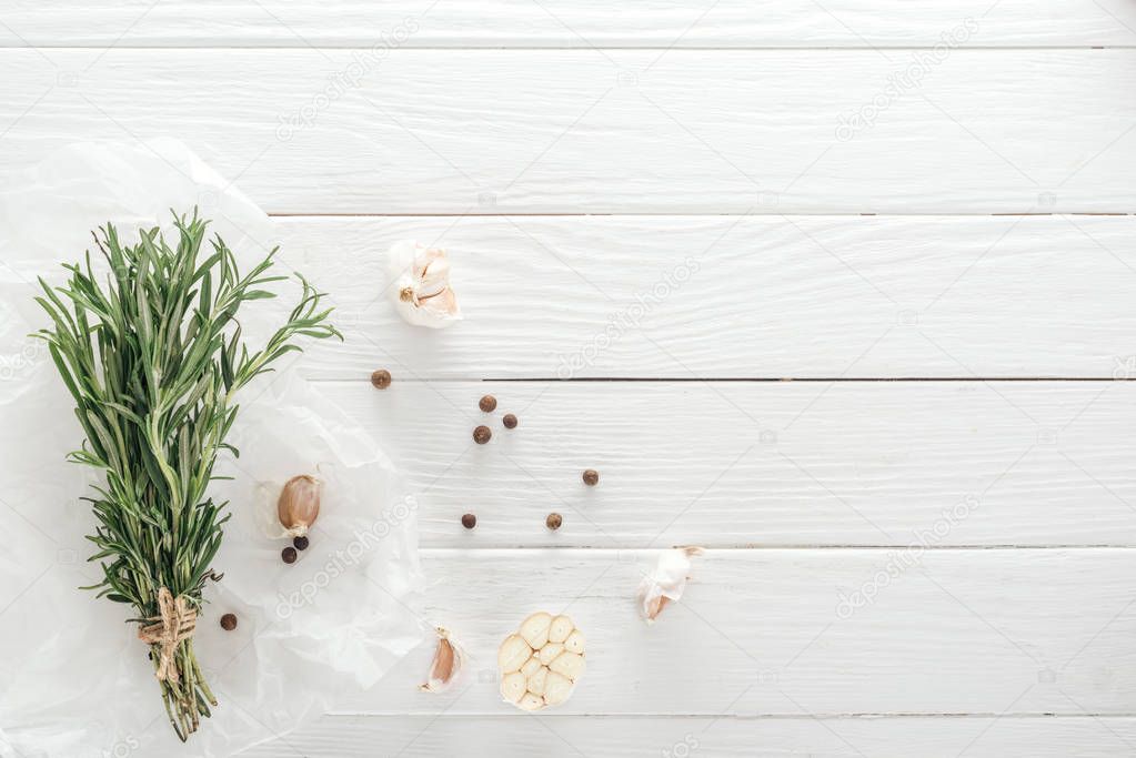 top view of garlic cloves, black pepper and rosemary on white wooden table