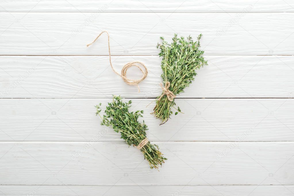 top view of green thyme near thread on white wooden table