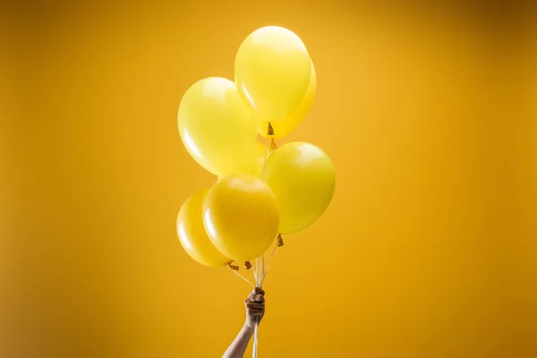 在黄色背景上手持节日明亮简约装饰气球的妇女的裁剪视图 — 图库照片
