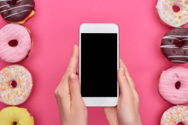 parlak pembe arka plan üzerinde lezzetli sırlı çörekler yakın boş ekran ile akıllı telefon tutan kadın kısmi görünümü