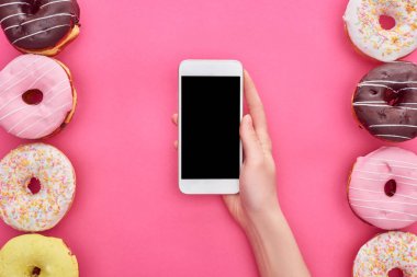 parlak pembe arka plan üzerinde lezzetli çörekler yakın boş ekran ile akıllı telefon tutan kadın kısmi görünümü