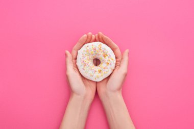 partial view of woman holding white glazed doughnuts with sprinkles on pink background clipart