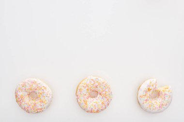 top view of sweet whole doughnuts with sprinkles near bitten one on white background clipart