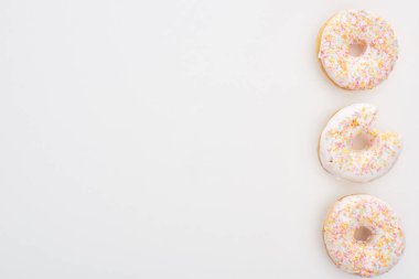 top view of whole doughnuts with sprinkles near bitten one on white background clipart