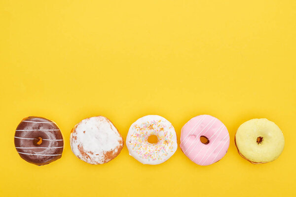 top view of tasty glazed doughnuts on bright yellow background