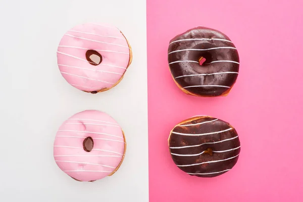 top view of glazed pink and chocolate doughnuts on white and pink colorful background