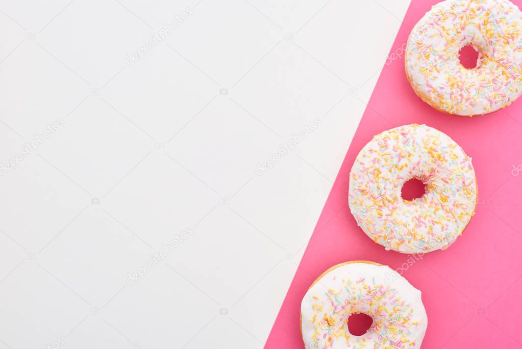 top view of glazed white doughnuts with sprinkles on white and pink background with copy space