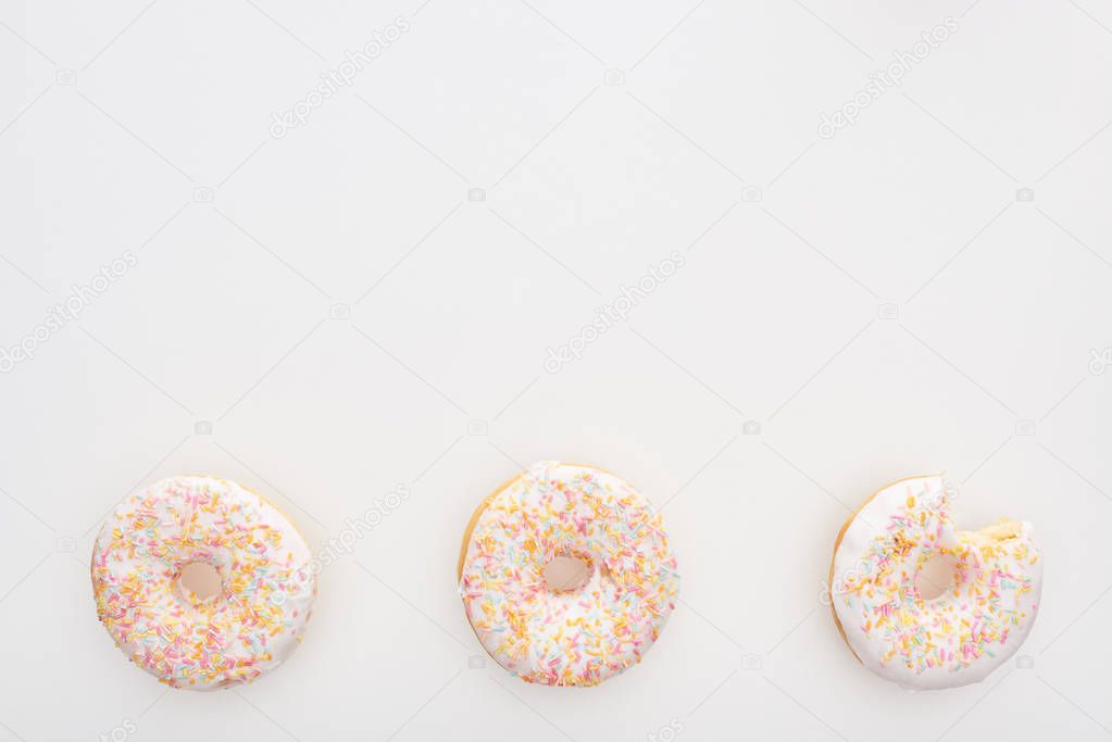 top view of sweet whole doughnuts with sprinkles near bitten one on white background