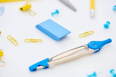 selective focus of blue compasses, eraser and paper clips mixed with yellow paper clips and pencil on white background clipart