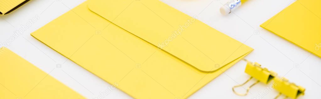 Panoramic shot of yellow envelope, pencil and paper clips on white background
