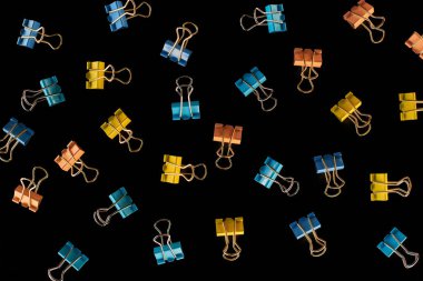 top view of scattered yellow, orange and blue paper clips isolated on black  clipart