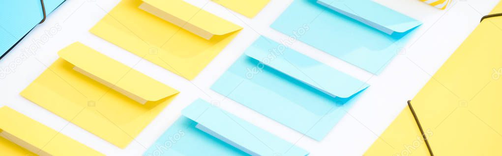 panoramic shot of yellow and blue folders and opened envelopes on white background