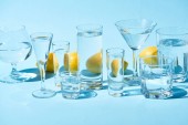 transparent glasses with water and whole lemons on blue background 