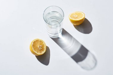 beyaz arka plan üzerinde limon yarıya yakın su ile şeffaf cam 