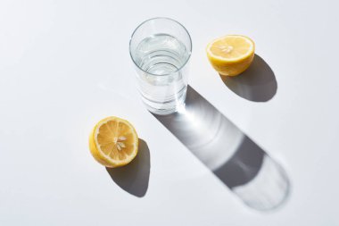 transparent glass with water near lemon halves on white background  clipart