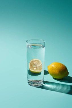 transparent glass with  water and lemon on turquoise background