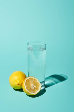 transparent glass with fresh water and bright lemon on turquoise background clipart